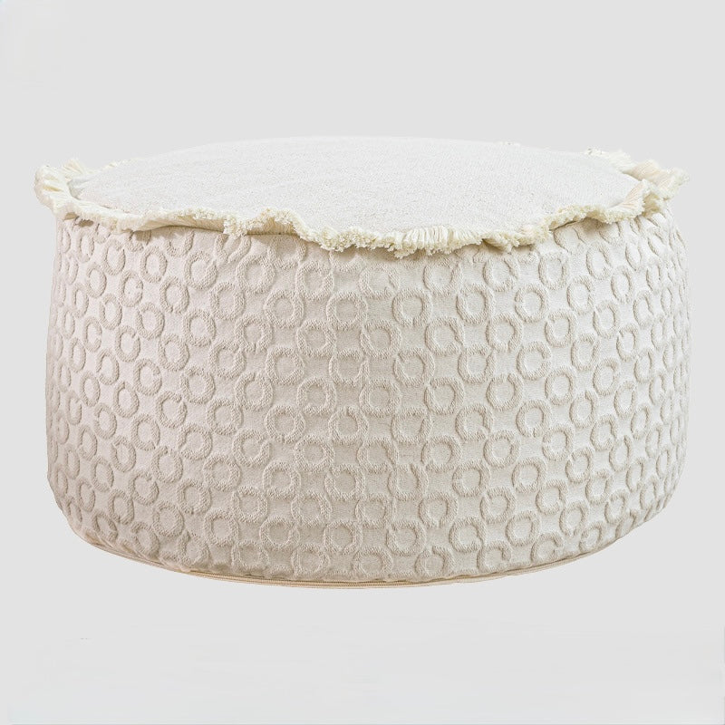 Circular tufted stool in a cream cotton blend with foam ball filling and decorative eyelash fringe.