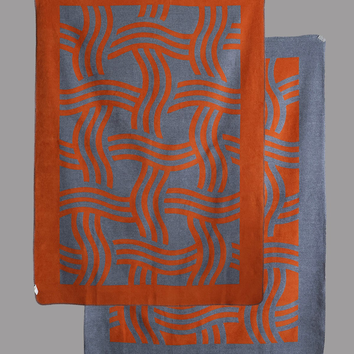 Full view of a geometric woven throw blanket featuring a bold mid-century pattern in orange and grey.