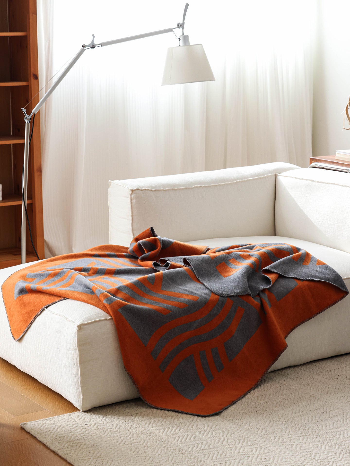 Mid-century inspired geometric throw in orange and grey draped over a chair in a calm, design-led living room.