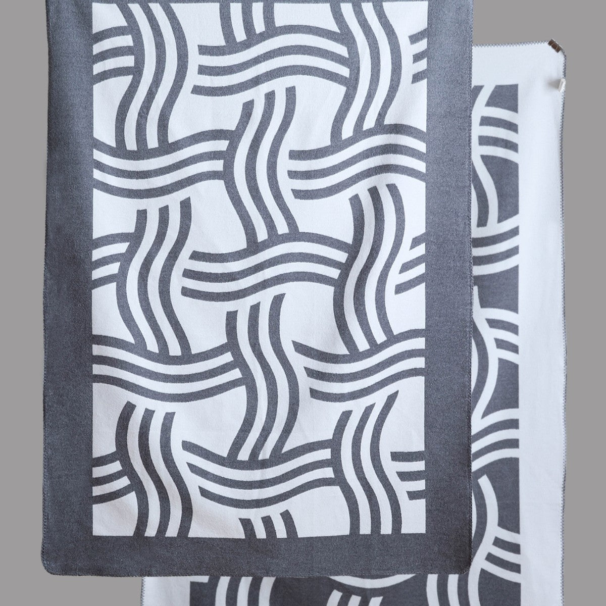 Reverse side of a geometric woven throw in soft grey and ivory, highlighting the clean graphic pattern.