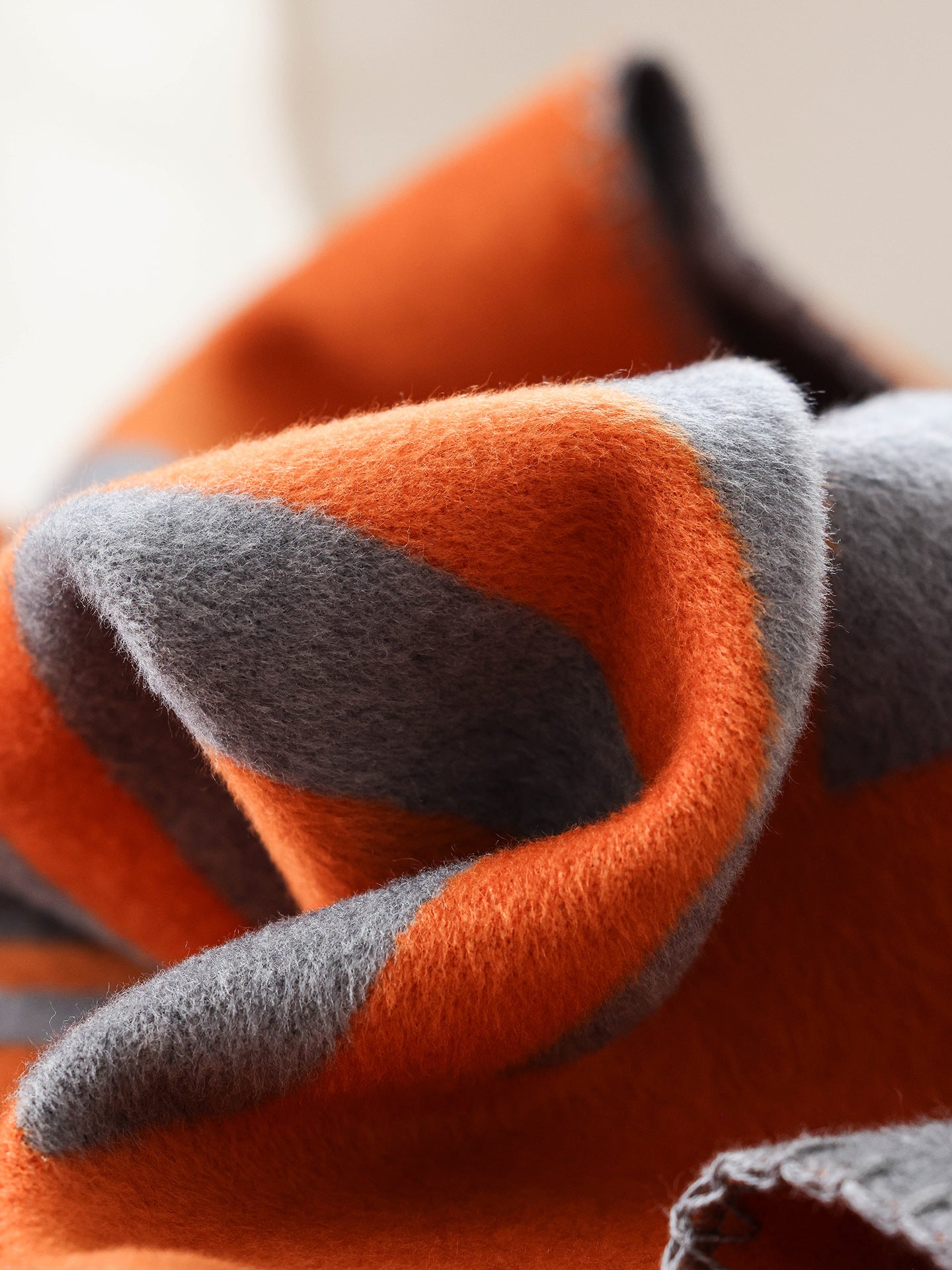 Folded geometric throw blanket showing soft woven texture and contrast between terracotta orange and graphite grey.