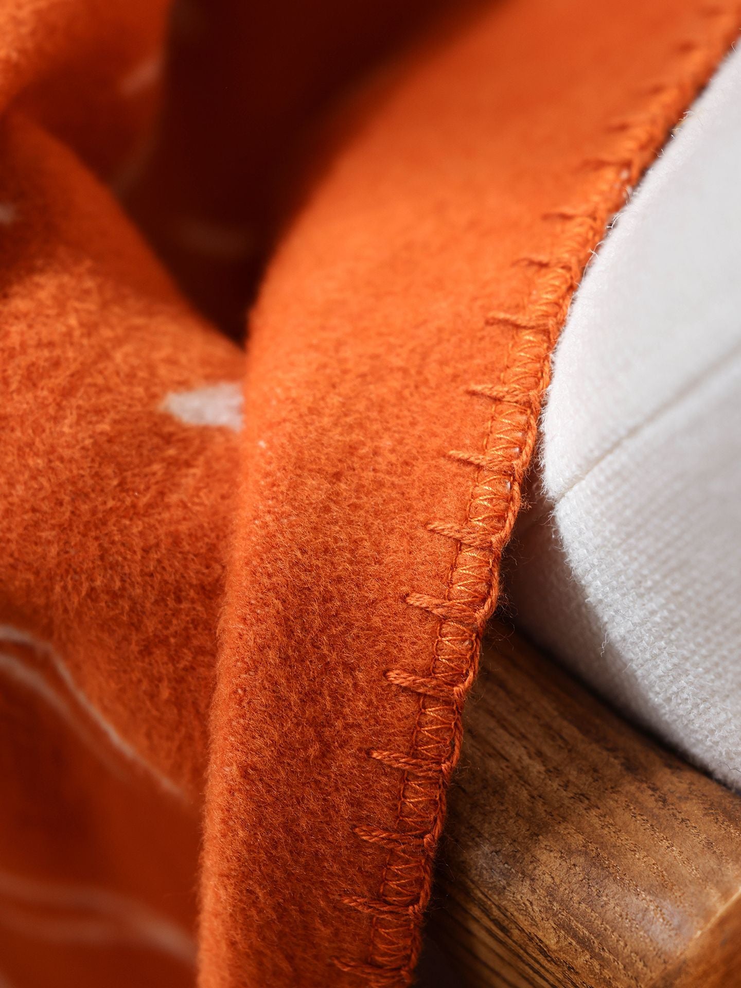 Close-up of hand-finished stitched edge on a geometric woven throw in warm terracotta and grey tones.