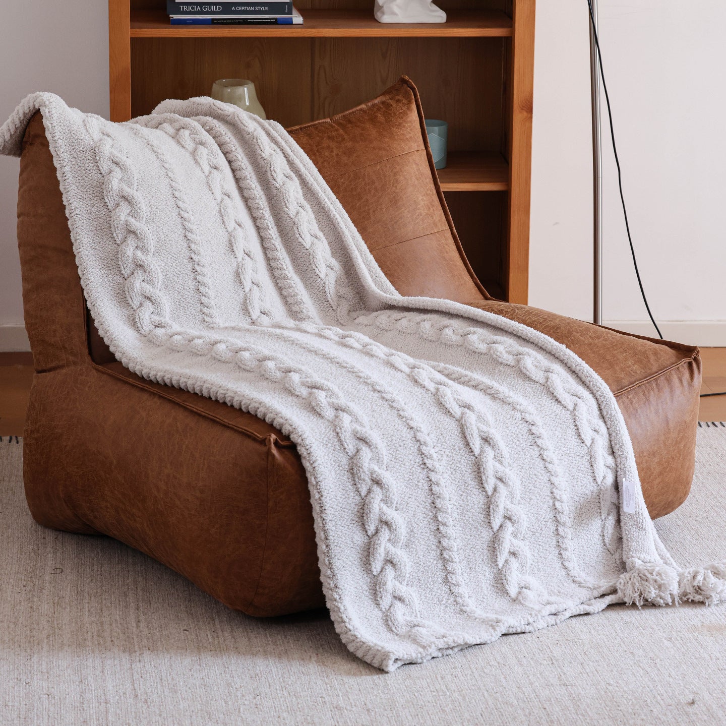A cozy reading nook featuring a white cable-knit throw draped over a brown leather chair, embodying Berriscent’s home with character vibe.